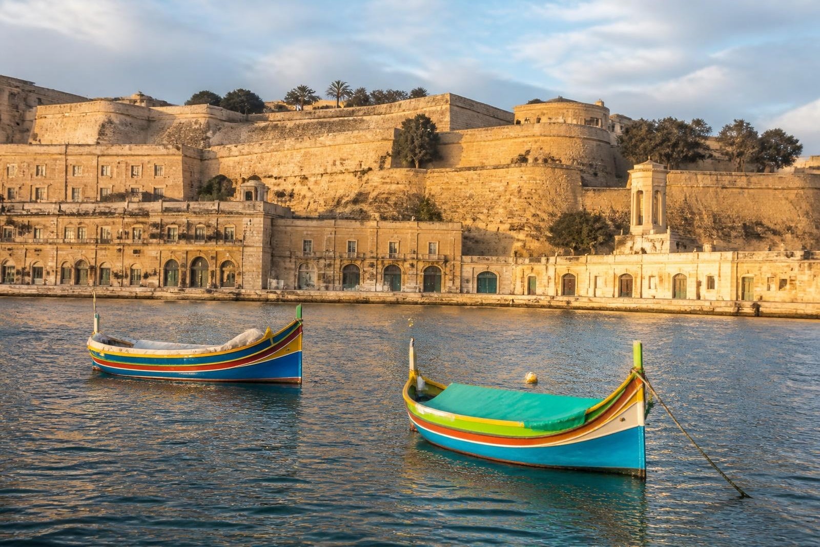 Historic limestone bastions above Valletta's harbour with traditional luzzu fishing boats
