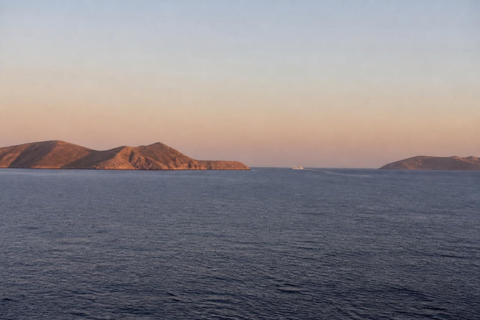 Calm Aegean sea at dusk with distant islands and a small ship on the horizon