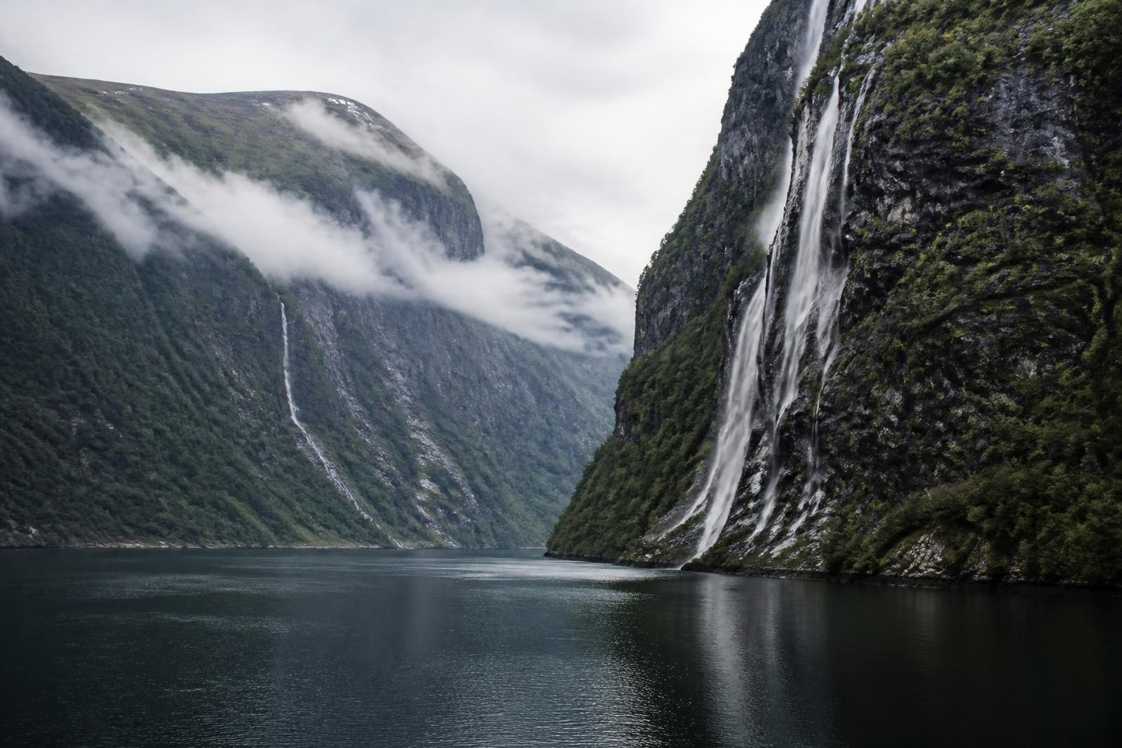 Steep cliffs and waterfalls above the still water of Geirangerfjord