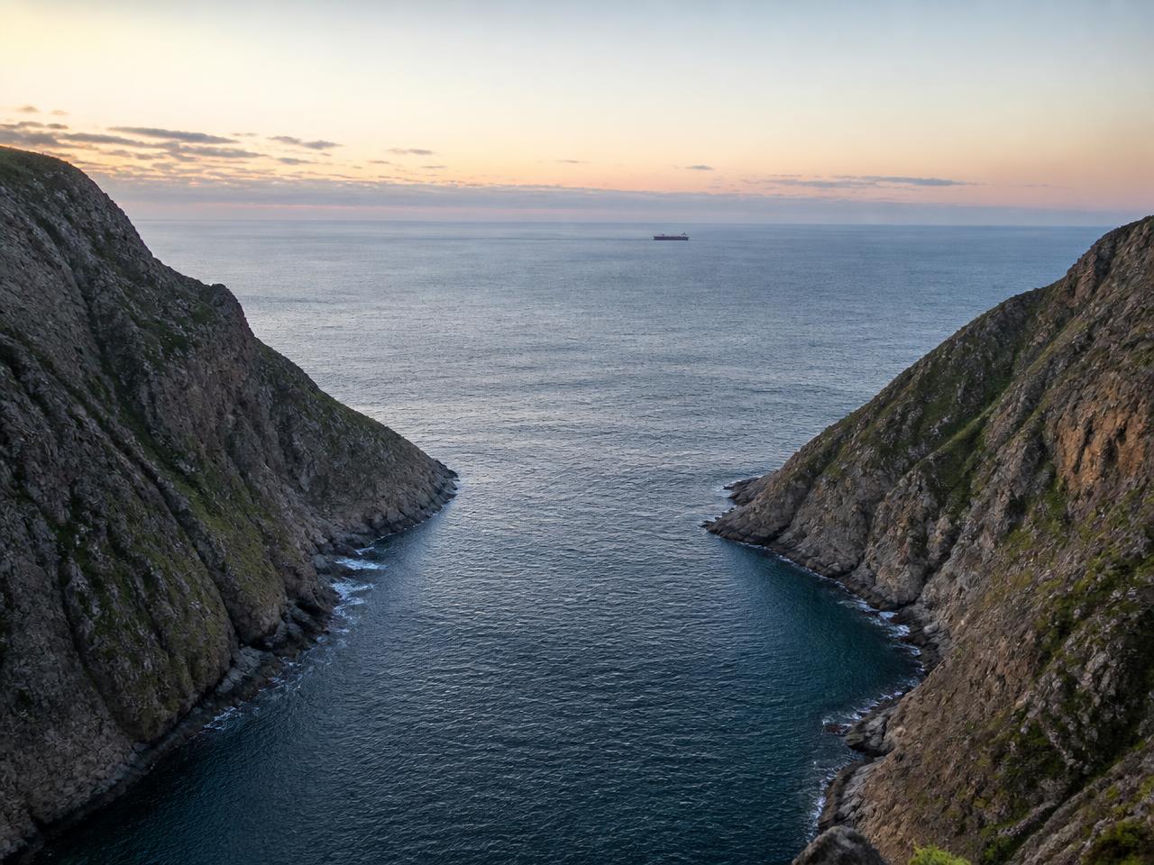 A narrow harbour entrance between steep headlands opening onto the sea at dawn
